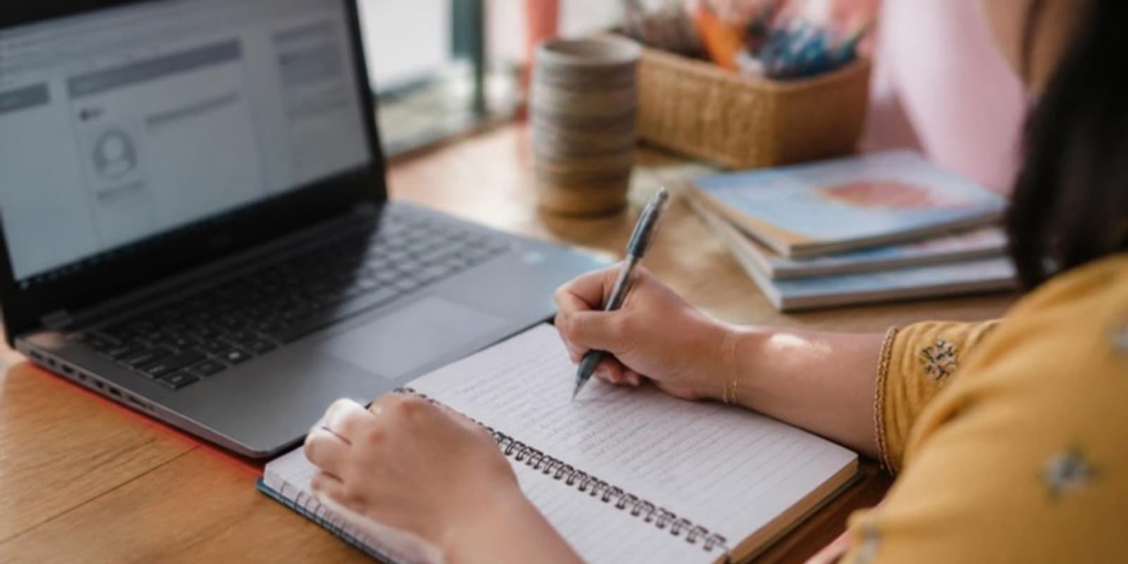 An educator writing lesson-plan notes beside her open laptop